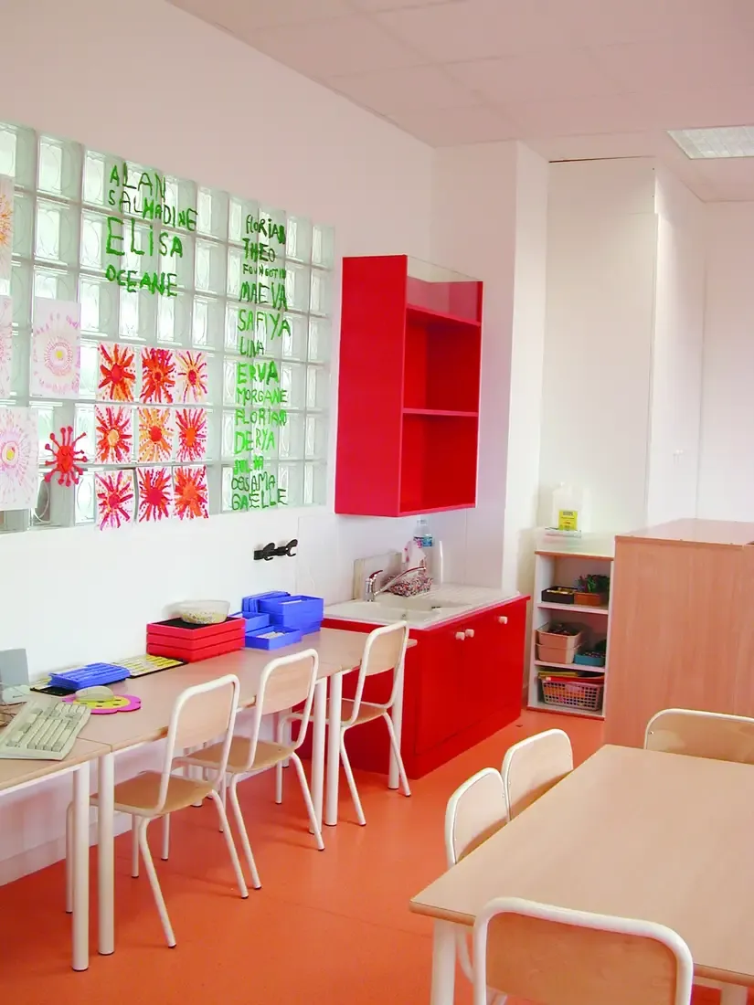 Une salle de classe à Montfermeil, meubles rouges et prénoms d'enfants sur les pavés de verre.