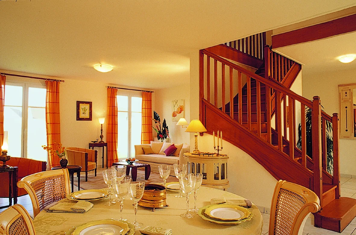 L'Aunaie, le rez-de-chaussée : table dressée, escalier de bois et rideaux orange.