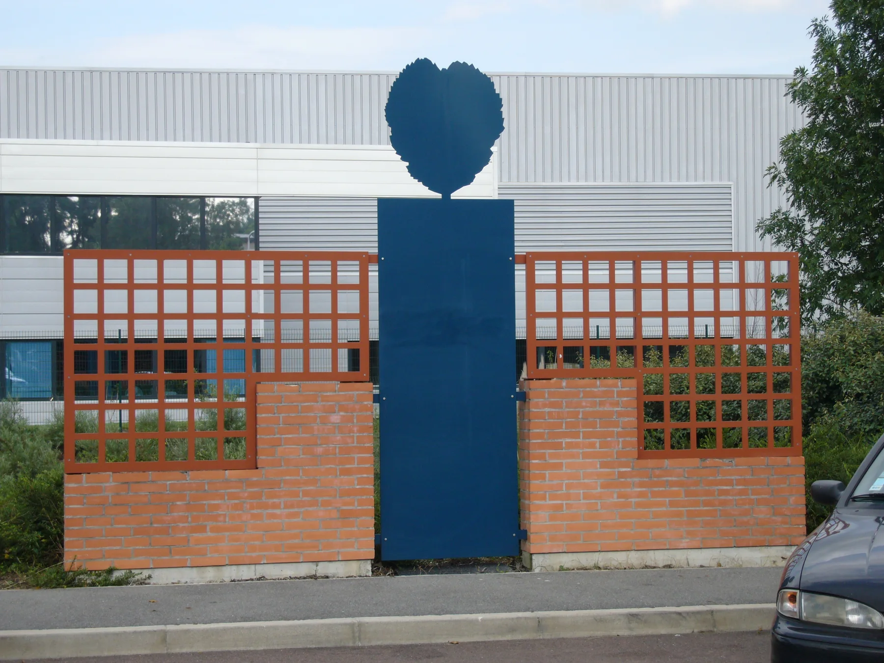 Le relais d'information réalisé : pilier bleu couronné de la petite feuille, murets de brique et treillis rouges.