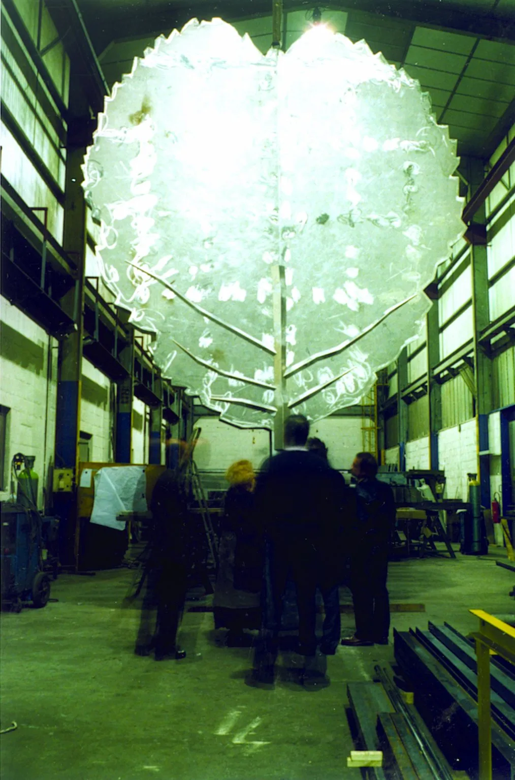 La grande feuille métallique suspendue dans l'atelier de fabrication, sous le regard de visiteurs.