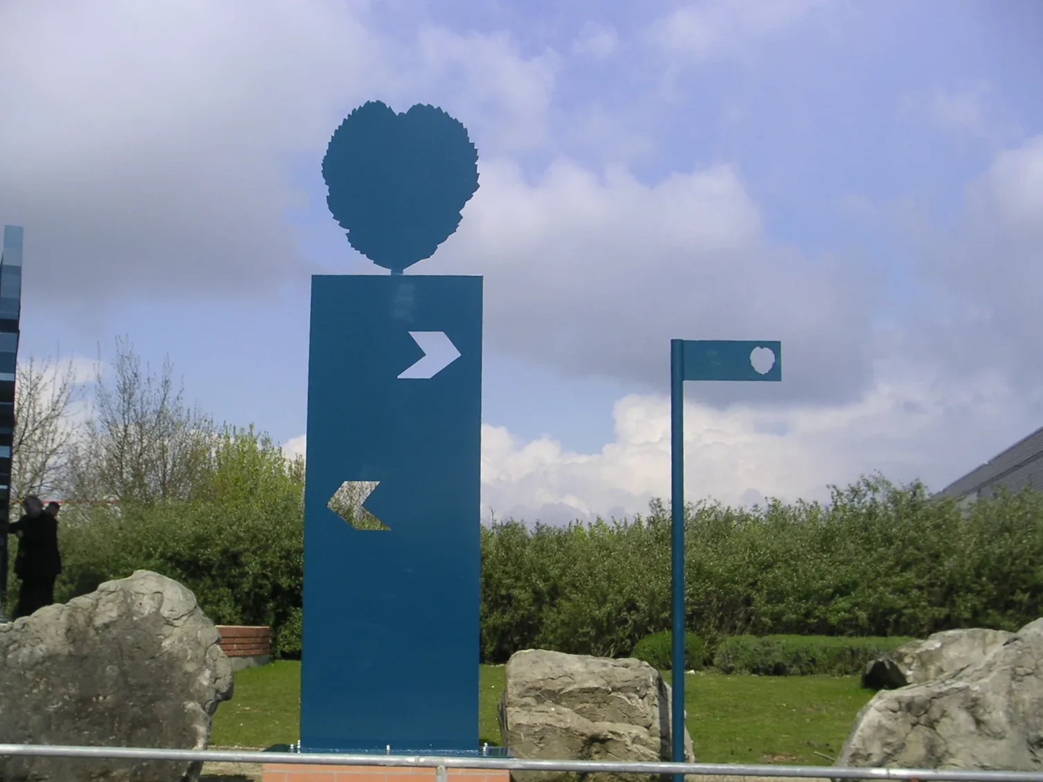 Le mât directionnel bleu, ses flèches découpées dans la tôle et sa feuille d'aulne, avec une plaque de rue à la petite feuille.