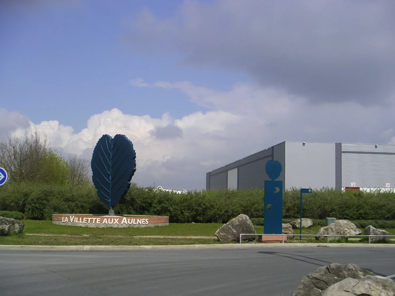 Le rond-point d'entrée en avril 2008 : la grande feuille sur son muret nominatif et, à droite, le mât directionnel.