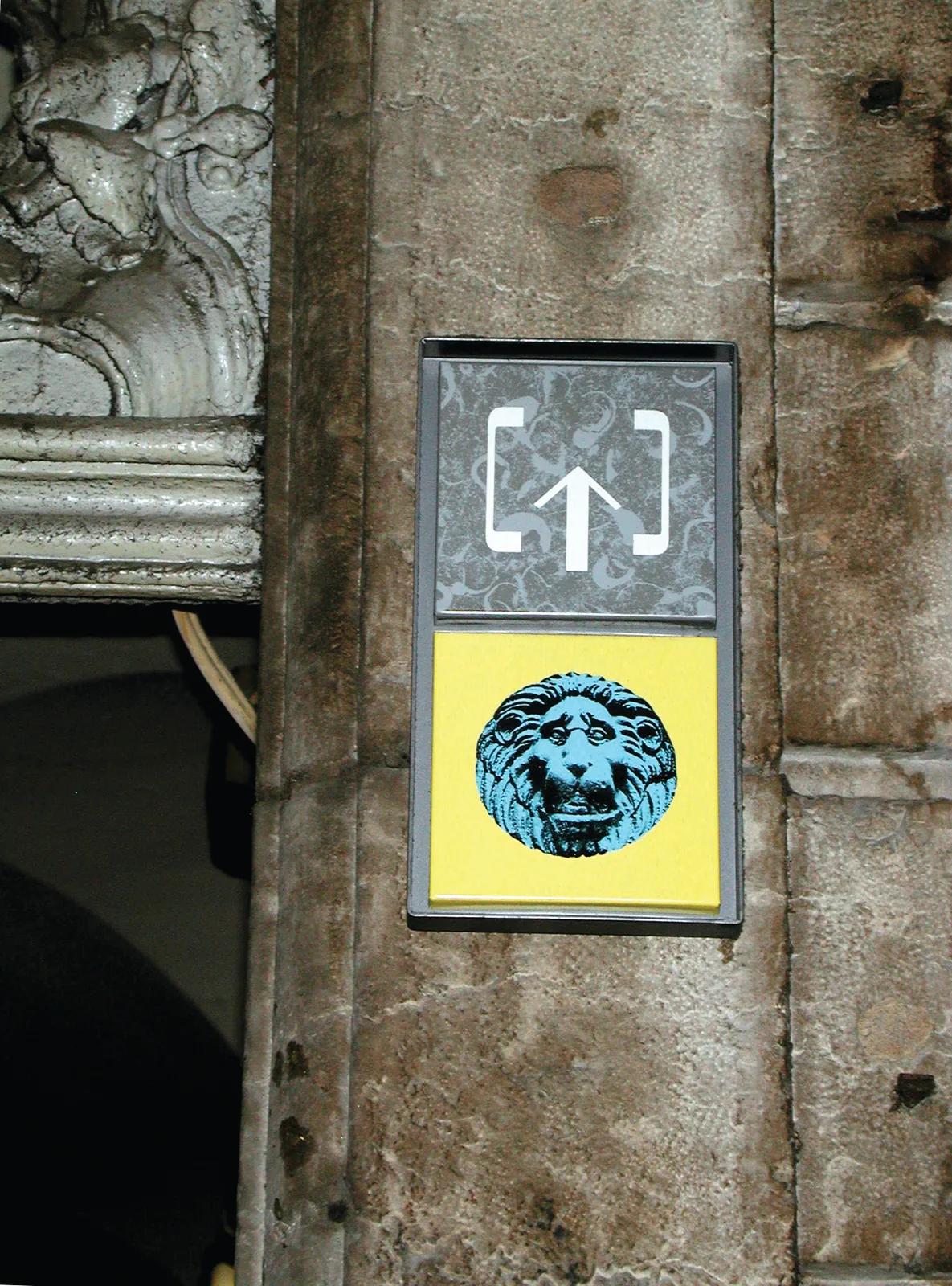 Pictogramme de traboule avec une flèche et une tête de lion, fixé sur une façade de pierre.