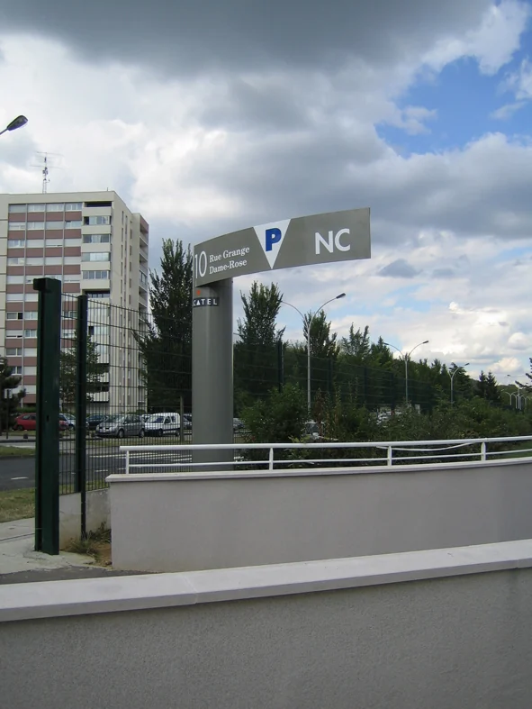 Poteau directionnel de parking « NC » au-dessus de la rampe, ciel nuageux.