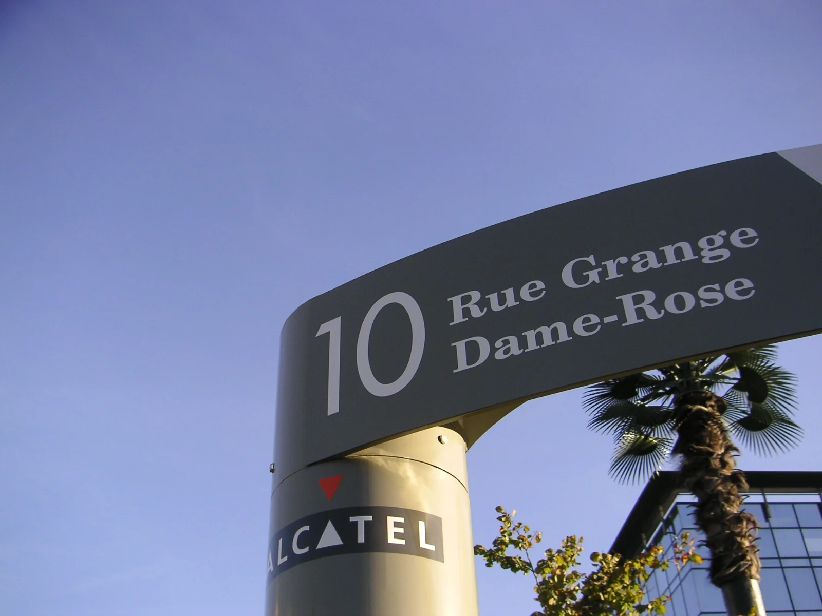 Vue en contre-plongée d'un bandeau cintré « 10 Rue Grange Dame-Rose » sur son mât marqué Alcatel, ciel bleu.