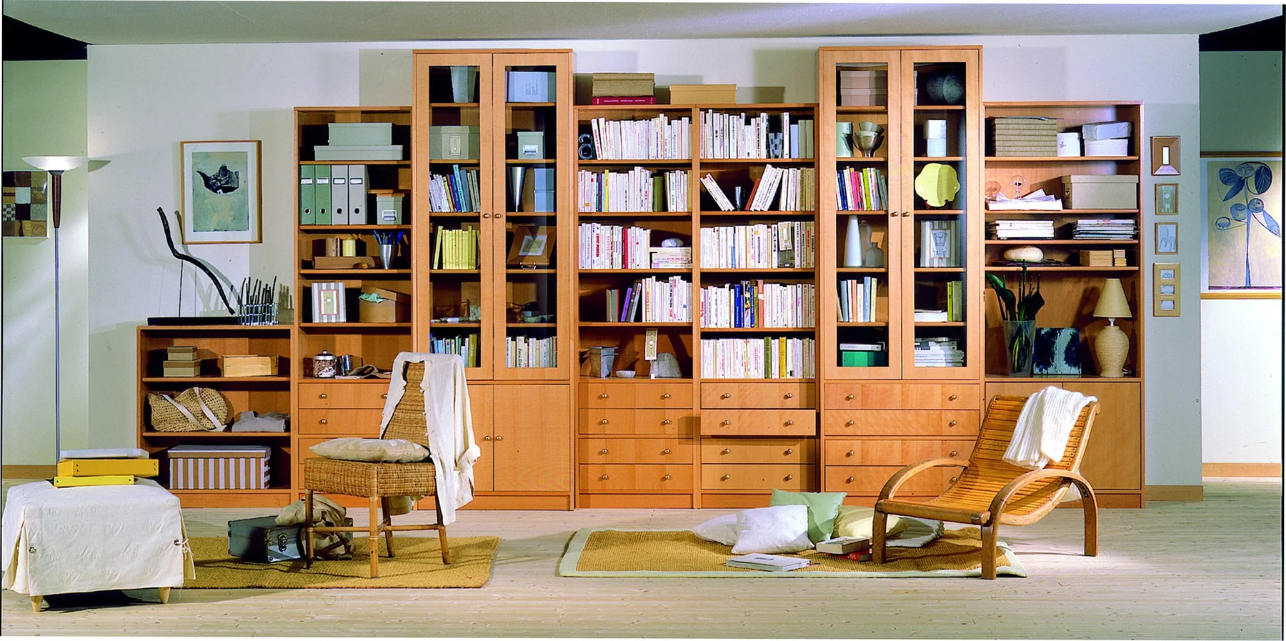Un mur entier de librairies en hêtre garnies de livres, avec fauteuils, tapis et lampadaire.