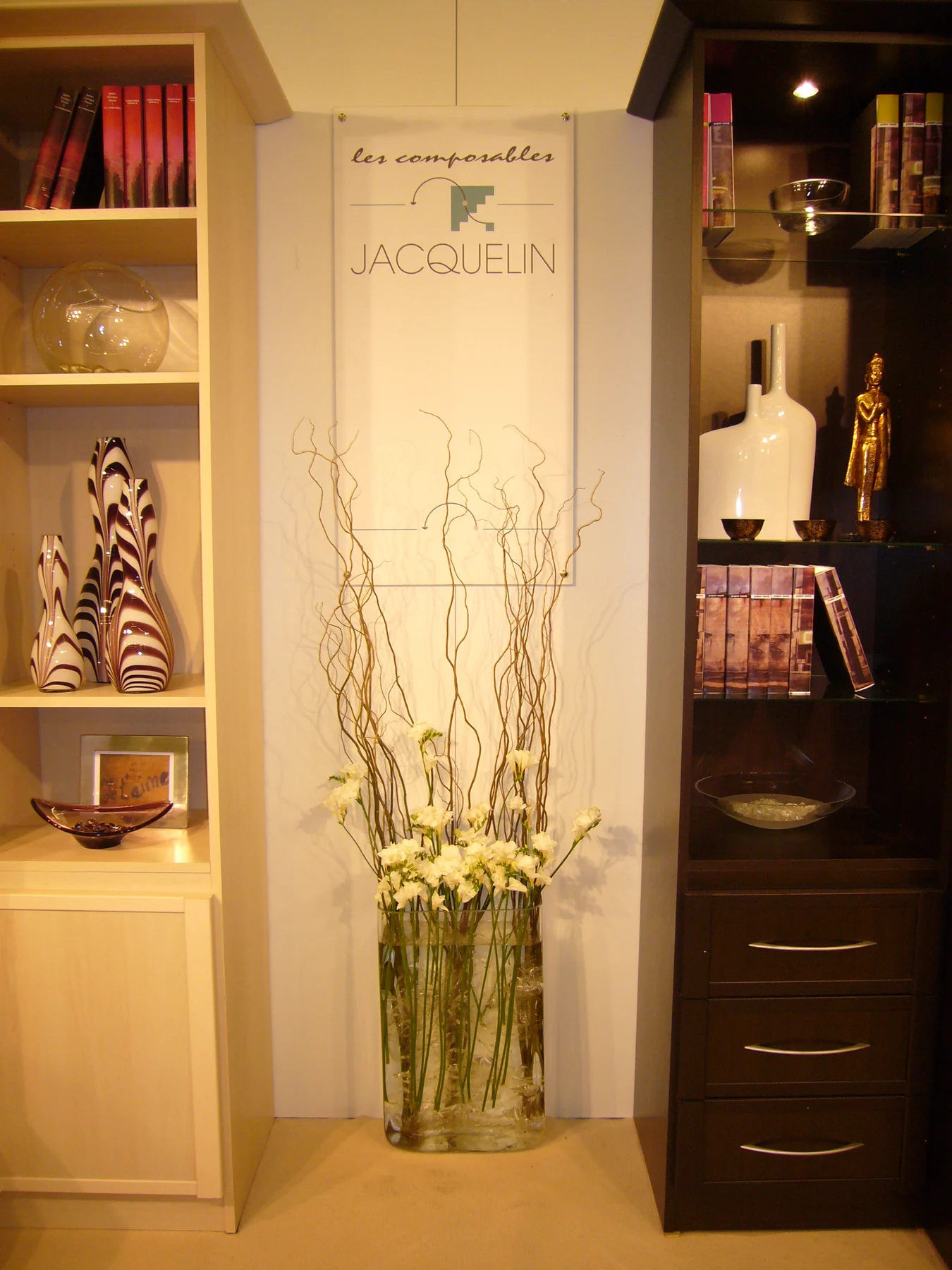 Sur le stand, un kakémono clair au logotype des Composables Jacquelin, entre deux colonnes de librairies garnies de vases et de livres.
