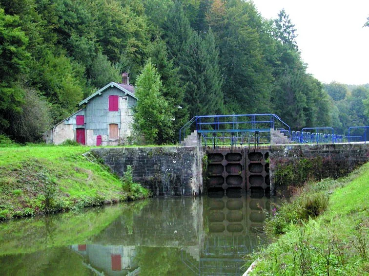 L'écluse 13 de Thiélouse, sa maison éclusière blanche aux volets rouges et sa passerelle bleue, entre deux rives boisées.