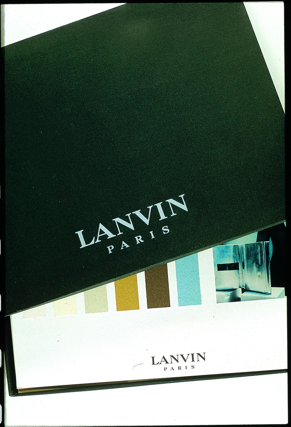 Coffret noir marqué Lanvin Paris entrouvert sur une planche de nuanciers : blanc, sable, ocre, brun, bleu glacier.